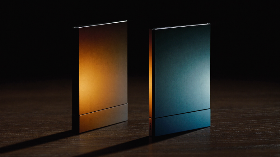 Two closed foldable phone silhouettes facing each other on dark walnut, one lit warm amber and one cool steel blue, representing a price and value comparison