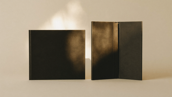 Editorial hero — two matte black closed foldable devices on cream studio backdrop with atmospheric warm amber accent light, representing the Galaxy Z Fold 8 vs Z Fold 8 Ultra buyer's choice.