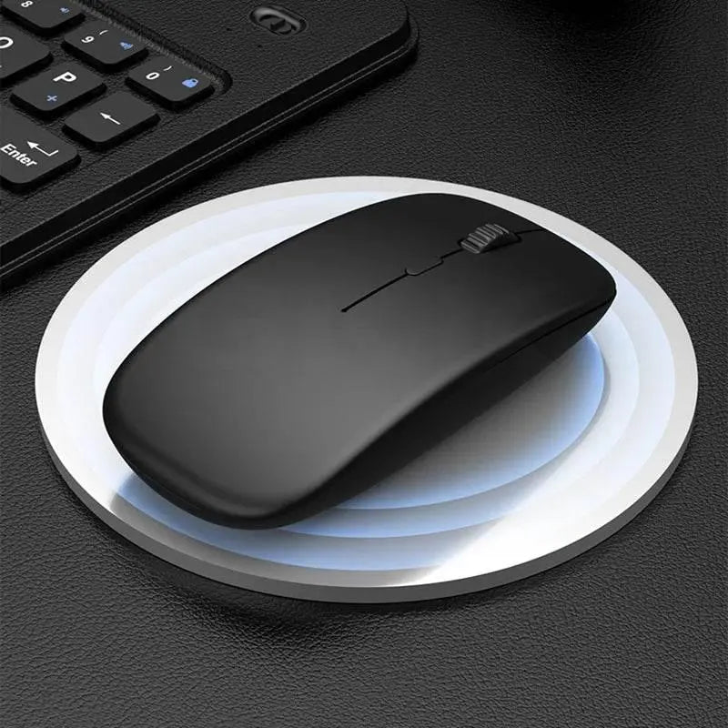 Sleek black wireless mouse on round white charging pad with part of black keyboard on black leather desk